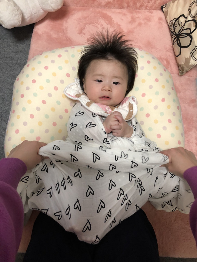 ママの膝で赤ちゃんのお尻を支えながら、赤ちゃんの足をあぐらか、裏を合わせて下の布を被せ、下半身をしっかりくるめるようにします